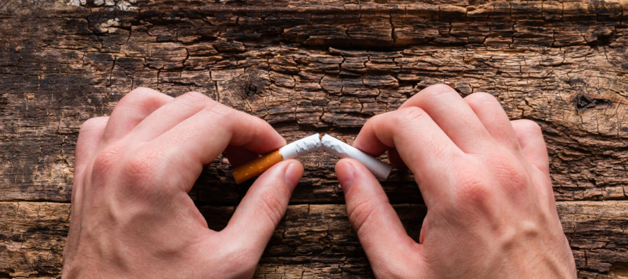 man breaks cigarette on a wooden background