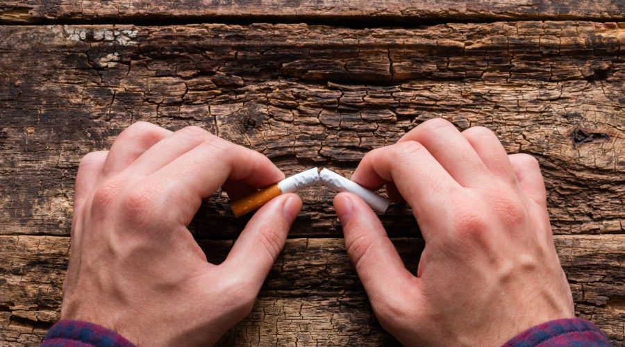 man breaks cigarette on a wooden background